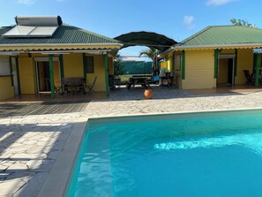 A pool area with a clear blue pool, a covered seating area, and two yellow buildings with green accents.