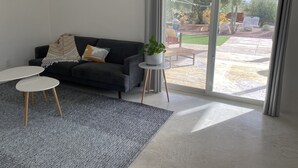 A modern living room with a dark sofa, two white round tables, a grey patterned rug, and a potted plant on a small white table. - Casita in the Catalina Foothills near Sabino Canyon, The Loop, restaurants, food (Tucson)