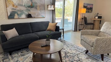 Una sala de estar con sofá, sillón, mesa de centro y un cuadro en la pared.