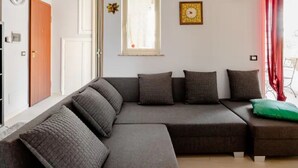 Ein modernes Wohnzimmer mit einer Eckcouch, einem kleinen Tisch und einem Fenster mit Vorhängen.