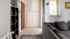 Ein Wohnzimmer mit Sofa, Heizkörper, Bücherregal und einer Tür zu einem anderen Raum.