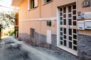 A narrow street with a building featuring a large window and a door, a small gate, and utility boxes on the wall. - Taormina Sea View Penthouse Apartment (Taormina)