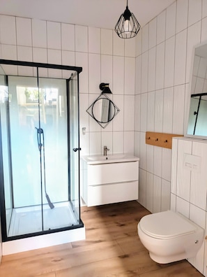 Un baño moderno con cabina de ducha de vidrio, un lavamanos blanco con espejo y un inodoro.