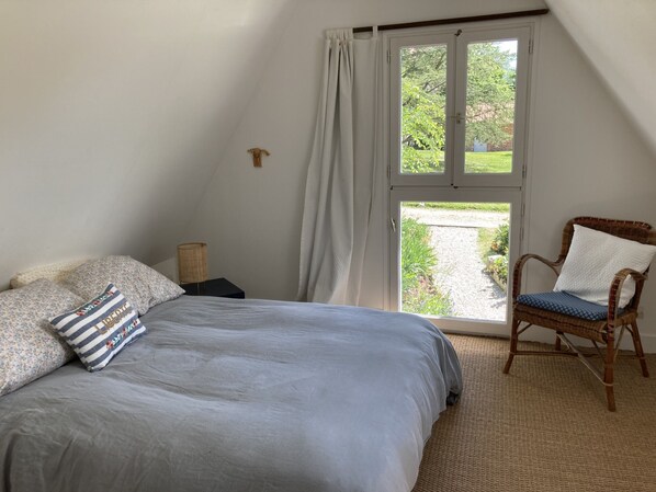 A bedroom with a bed, a chair, a nightstand, and a window with curtains. - La Maison de Marguerite, in the meadow of Varengeville (Varengeville-sur-Mer)