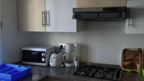 Une cuisine avec des meubles blancs, un four à micro-ondes, une machine à café et une cuisinière à gaz.