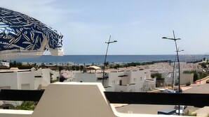 Un balcon avec vue sur la mer et les bâtiments. On y trouve une chaise et une table.