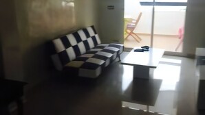 Un salon moderne avec un canapé à carreaux noirs et blancs, une petite table basse blanche et une porte-fenêtre coulissante donnant sur un espace extérieur.