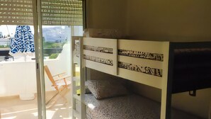 Une chambre avec des lits superposés, une porte-fenêtre coulissante donnant sur un espace extérieur et une vue sur un paysage montagneux.