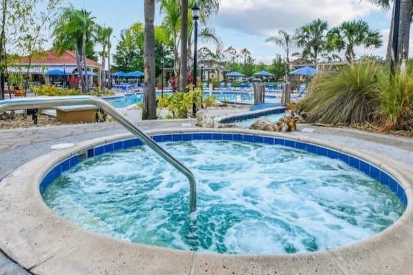 Un jacuzzi con escalera metálica, rodeado de palmeras y una zona de piscina con sillones de descanso.