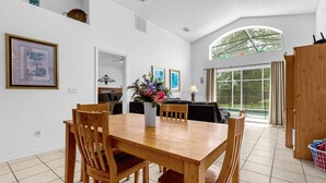 Un comedor amplio con una mesa y sillas de madera, un florero con flores y vistas al exterior a través de un ventanal grande.