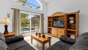 Una sala moderna con televisor, mueble de entretenimiento de madera y vista a la piscina.