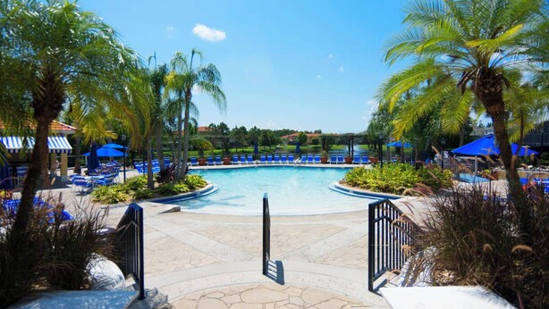 Zona de piscina en un resort, con palmeras, sillas de descanso y sombrillas.
