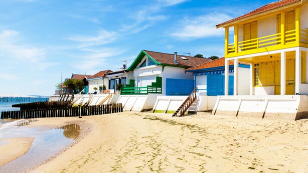 A beach with colorful buildings, a wooden fence, and a clear blue sky. - Charming house in Biscarrosse Plage with heated swimming pool  (Nouvelle-Aquitaine)