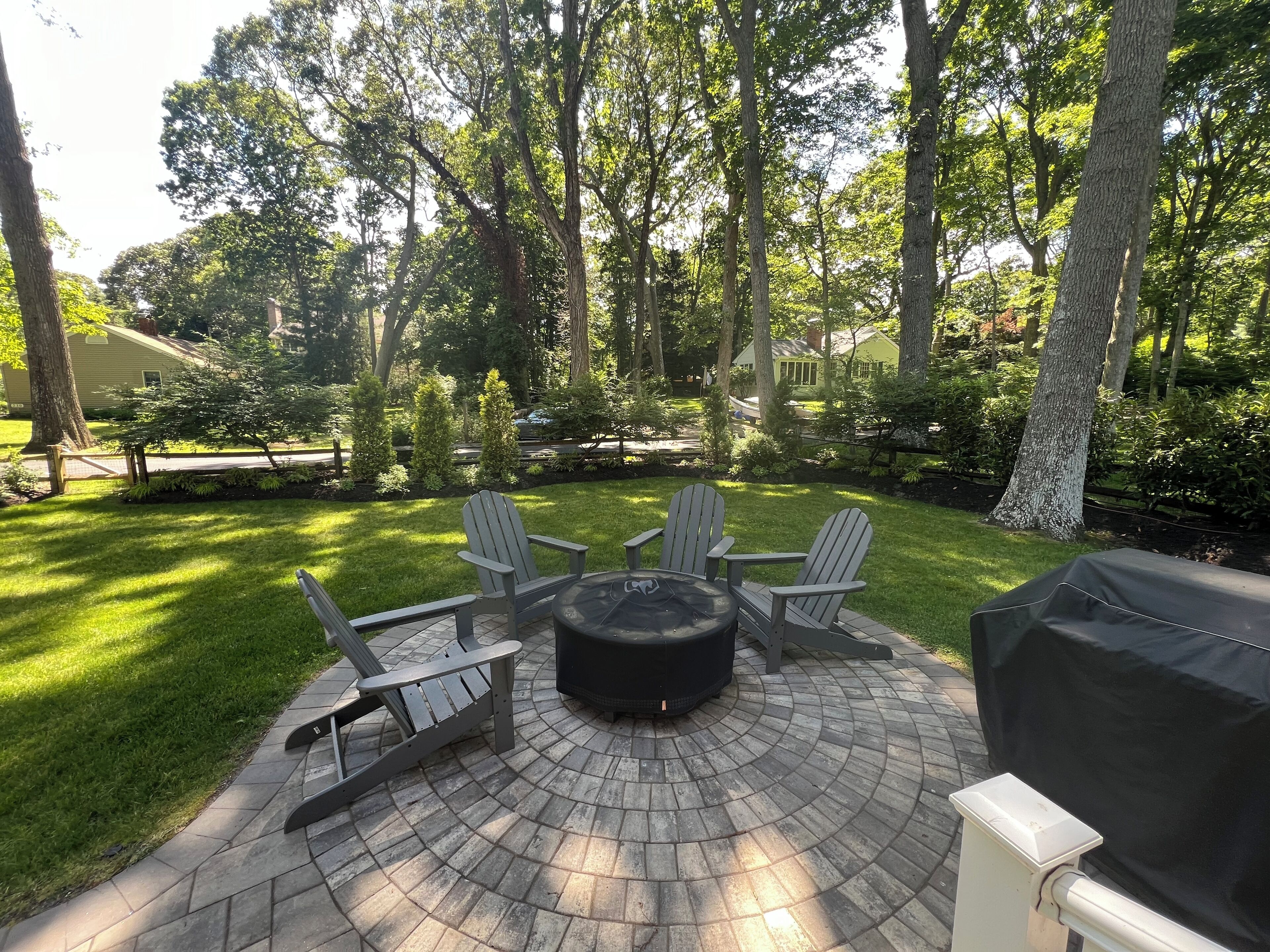 A patio area with a circular fire pit, four Adirondack chairs, and a grill.