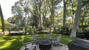 Un patio con un pozo de fuego circular, cuatro sillas Adirondack y una parrilla.