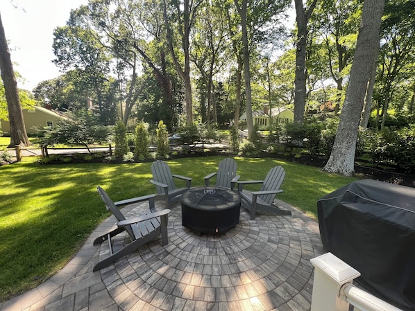 A patio area with a circular fire pit, four Adirondack chairs, and a grill. - Walk to private bay beach, close to Greenport, wineries, golf! Premier Host home (East Marion)