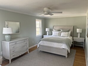 Une chambre à coucher comprenant un lit, des tables de chevet, une commode, un ventilateur de plafond et une fenêtre.