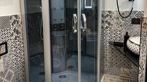 A modern bathroom with a glass-enclosed shower, a white sink, and patterned tiles. - Designer apartment in the historic center (Palermo)