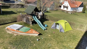 A grassy area with a small wooden playhouse, a green slide, a tent, and a boat. - Small vacation apartment (65m²) with "beautiful view" Garden with playground (Nieder-Werbe)