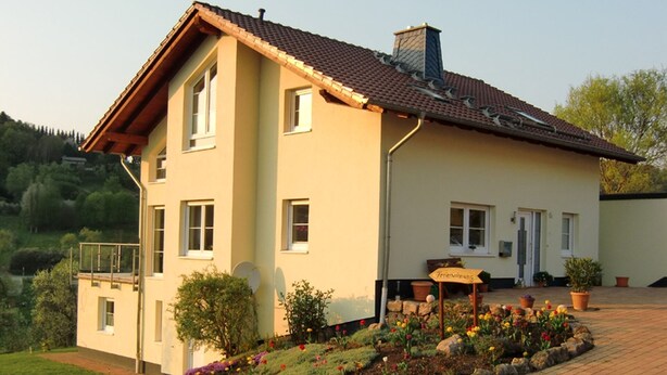 A two-story house with a tiled roof, a balcony, and a flower garden in front. - Small vacation apartment (65m²) with "beautiful view" Garden with playground (Nieder-Werbe)