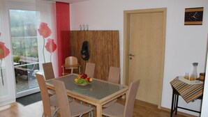 A dining area with a glass table, four chairs, a wooden door, and a clock on the wall. - Small vacation apartment (65m²) with "beautiful view" Garden with playground (Nieder-Werbe)