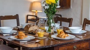 Ein Esstisch mit Croissants, Orangensaft und einer Blumenvase.