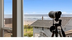 Un telescopio sobre un trípode que da vista a una playa con casas al fondo.