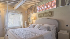 A bedroom with a large bed, a nightstand, a lamp, and a window with curtains.