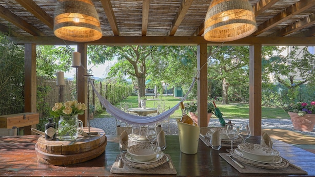 An outdoor dining area with a wooden pergola, hanging wicker lamps, and a table set for a meal.