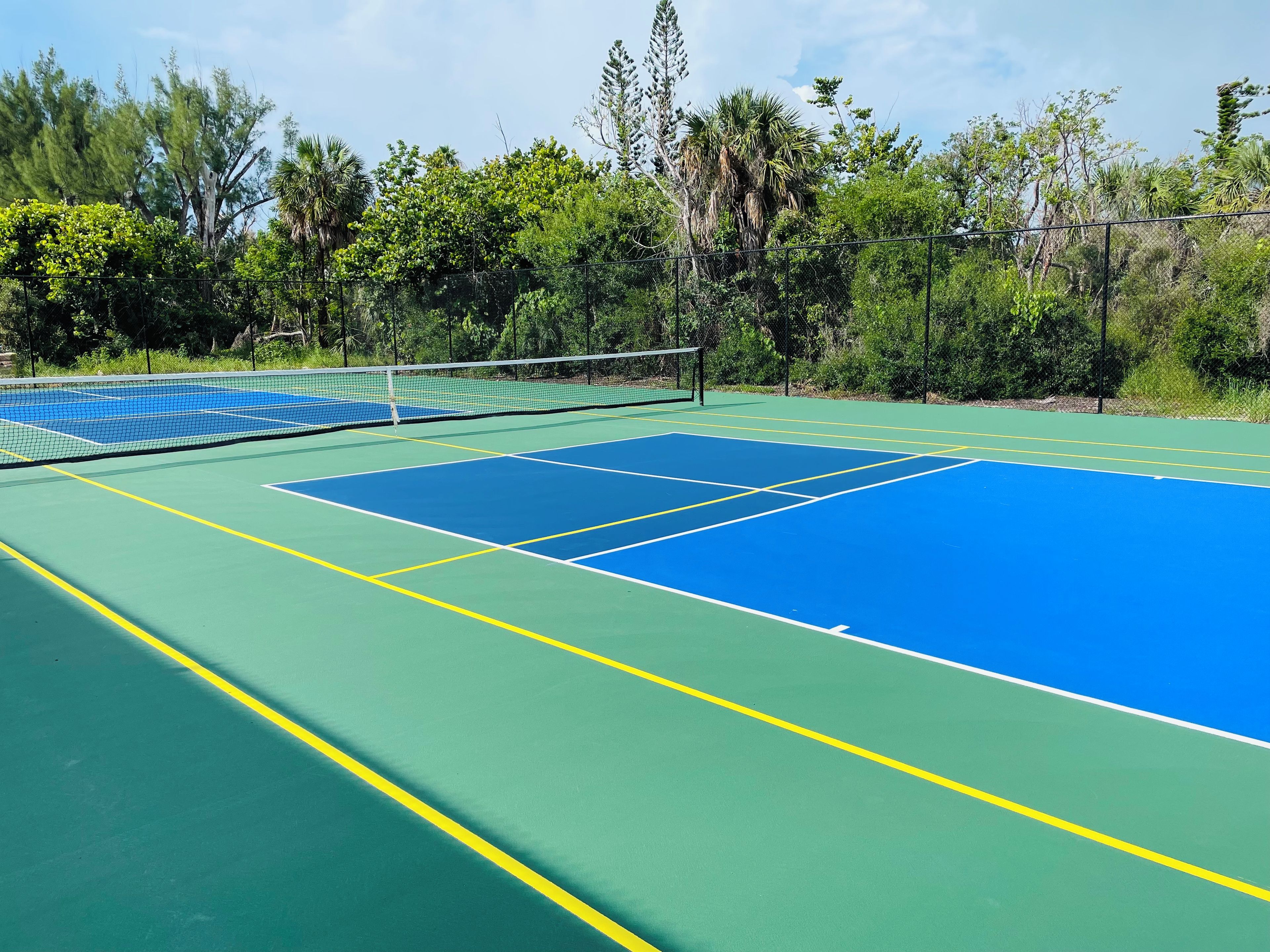 A tennis court with a net, surrounded by trees and greenery.