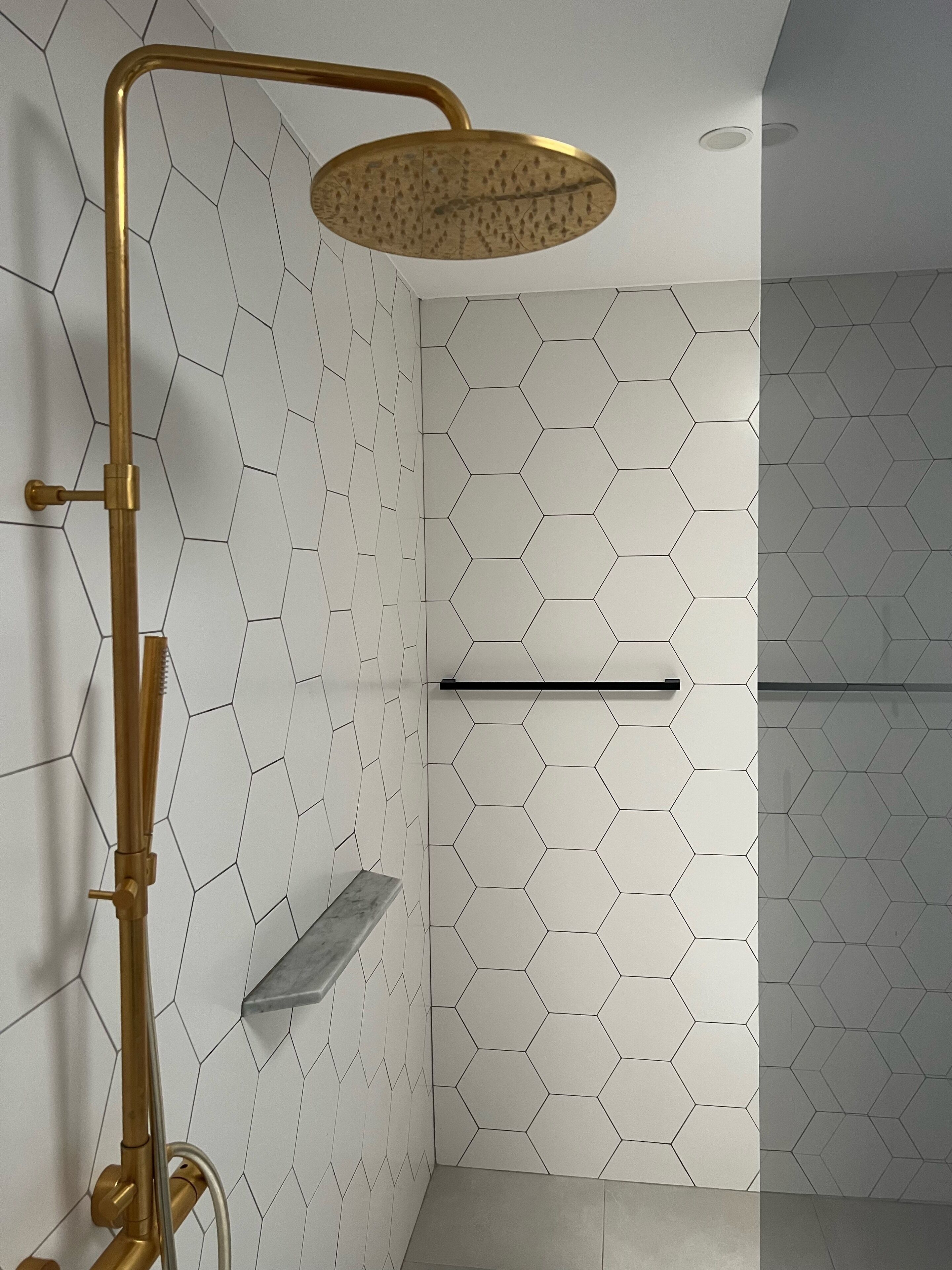 A shower with a gold showerhead and a hexagonal tile pattern on the walls.