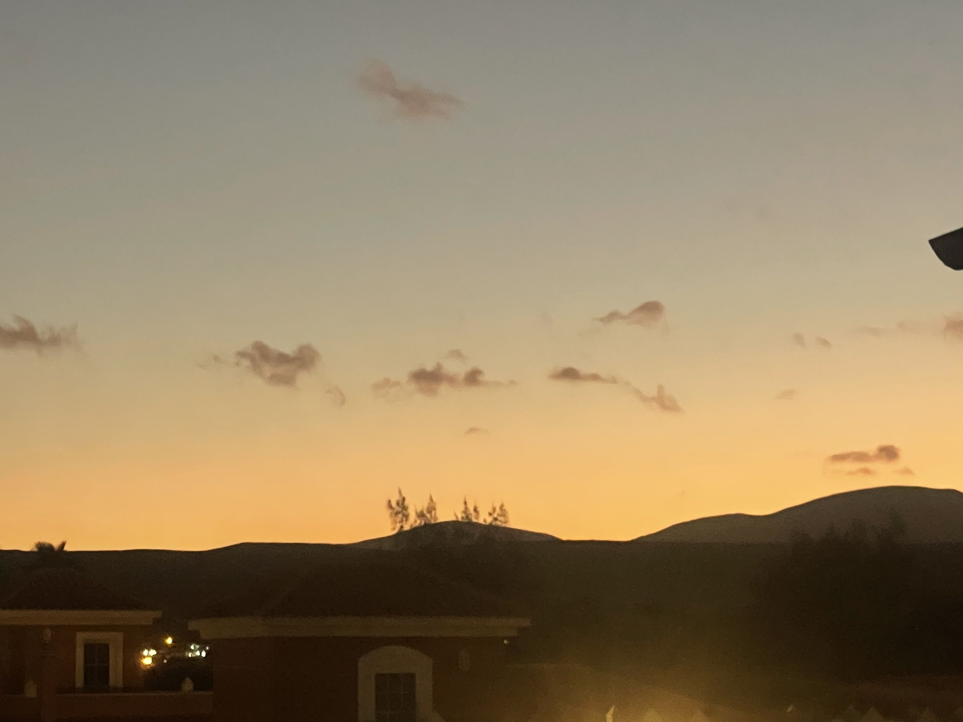 Solnedgang over et bygningssilhuet og fjerne bakker.