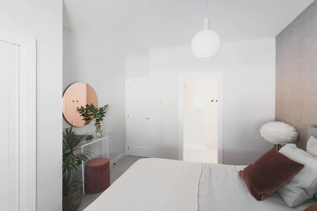 A modern bedroom with a bed, a round mirror, a potted plant, and a white door.