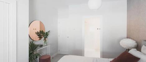 A modern bedroom with a bed, a round mirror, a potted plant, and a white door.