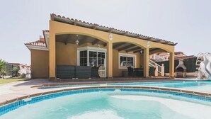Un espace aménagé au bord de la piscine, comprenant un patio couvert, une piscine et une cheminée en pierre.