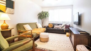 A living room with a sofa, armchair, ottoman, television, and a ceiling fan. - Mid-Century Modern Retro Beach House (Caloundra Region)