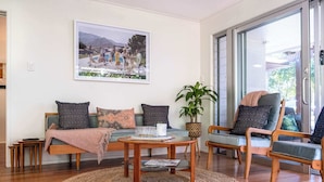 A living room with a sofa, armchairs, a coffee table, and a large window. - Mid-Century Modern Retro Beach House (Caloundra Region)