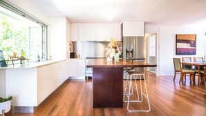 A modern kitchen with a central island, white cabinetry, and a stainless steel refrigerator. - Mid-Century Modern Retro Beach House (Caloundra Region)