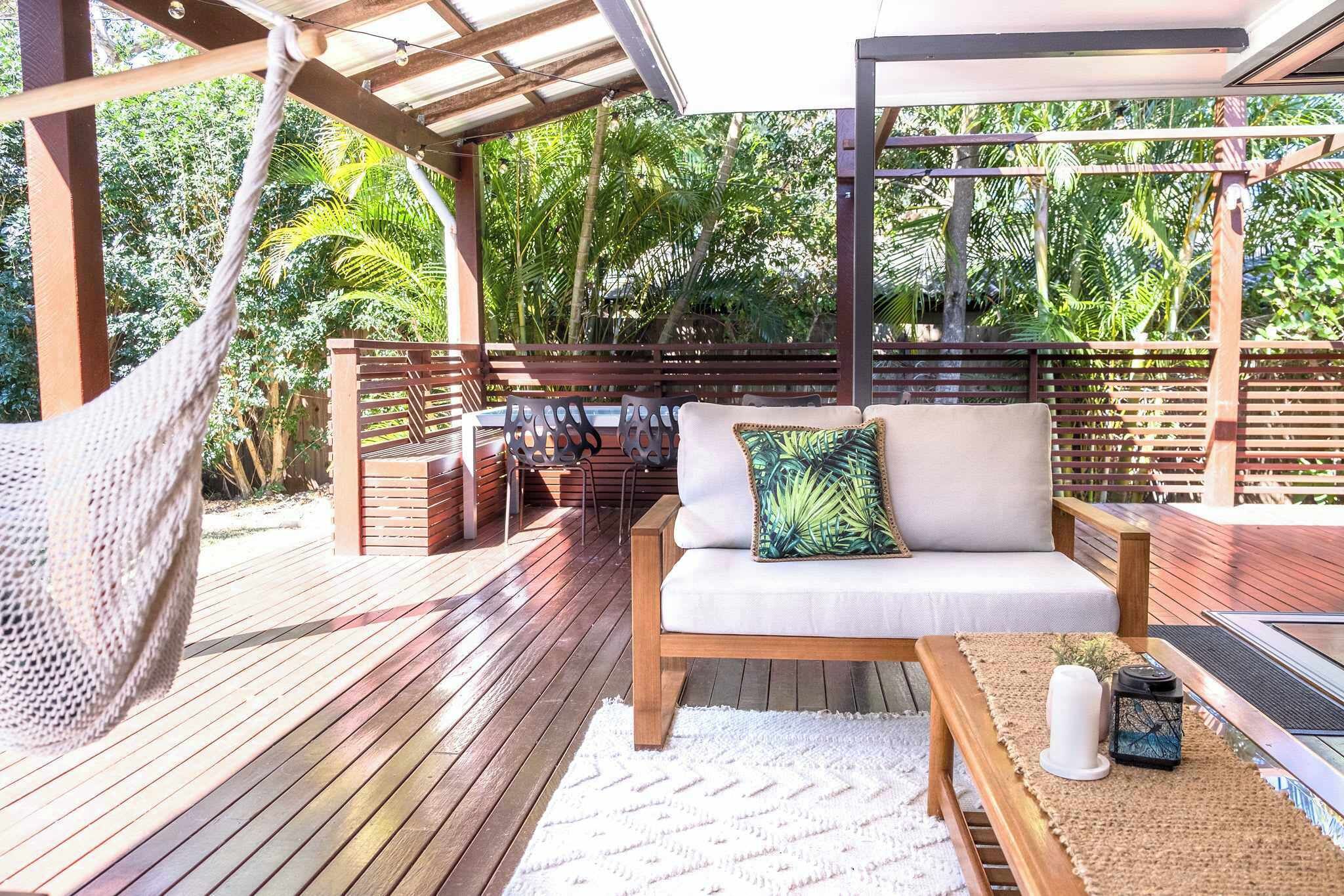 A wooden deck with a hammock, a sofa with a tropical pillow, and a table with a candle and lantern.