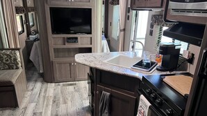Cocina compacta para autocaravana con televisión integrada, un lavamanos y una cafetera.