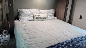 Una cama bien hecha con una colcha acolchada, un almohadón con la palabra 'hope' y su definición, y un ventilador en el suelo junto a la cama.