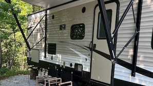Una caravana con un toldo grande, una plataforma escalonada y una pequeña mesa de madera con sillas.