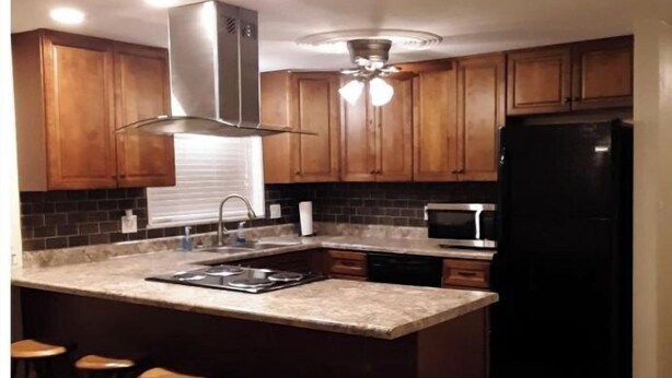 A kitchen with wooden cabinets, a black refrigerator, a microwave, a stove, and a ceiling fan. There are three stools at the island. - Relax in the country at Countryside Villas! - Villa A (Jackson)