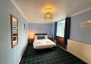 A hotel room with a bed, a nightstand, a lamp, a window with curtains, and a radiator. - Spacious 3BR Cottage in Beautiful Rural Setting - Pass the Keys (Castle Douglas)