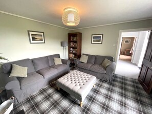 Ein Wohnzimmer mit grauem Sofa, passendem Hocker, Stehlampe und Bücherregal.