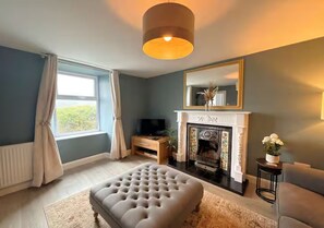 A living room with a fireplace, a television, and a large ottoman. - Spacious 3BR Cottage in Beautiful Rural Setting - Pass the Keys (Castle Douglas)