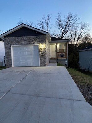 Une maison à deux étages avec une façade en pierre, un garage et un porche à l’avant.