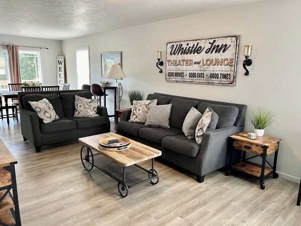 Un salon comprenant deux canapés, une table basse, une table d’appoint avec une plante, et une enseigne murale indiquant : « Whistle Inn, théâtre et salon ».