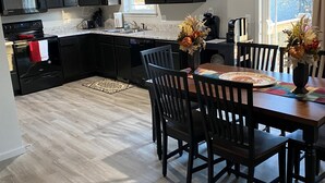 Una cocina moderna con armarios oscuros, una mesa de comedor con sillas y vistas al exterior a través de una ventana.