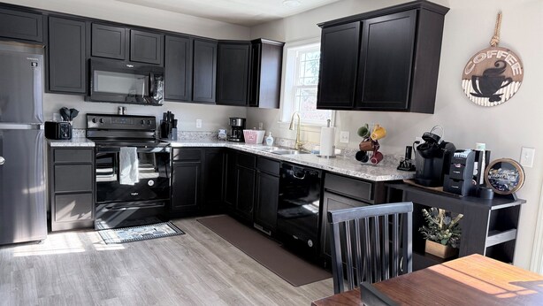 Una cocina moderna con armarios oscuros, electrodomésticos de acero inoxidable, una encimera de granito y un comedor con mesa y sillas de madera.